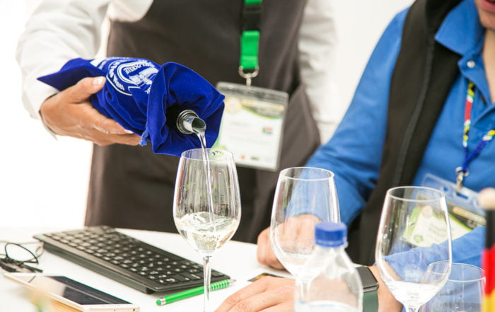 Someone serving white wine. The bottle is in a blue CMB branded bag